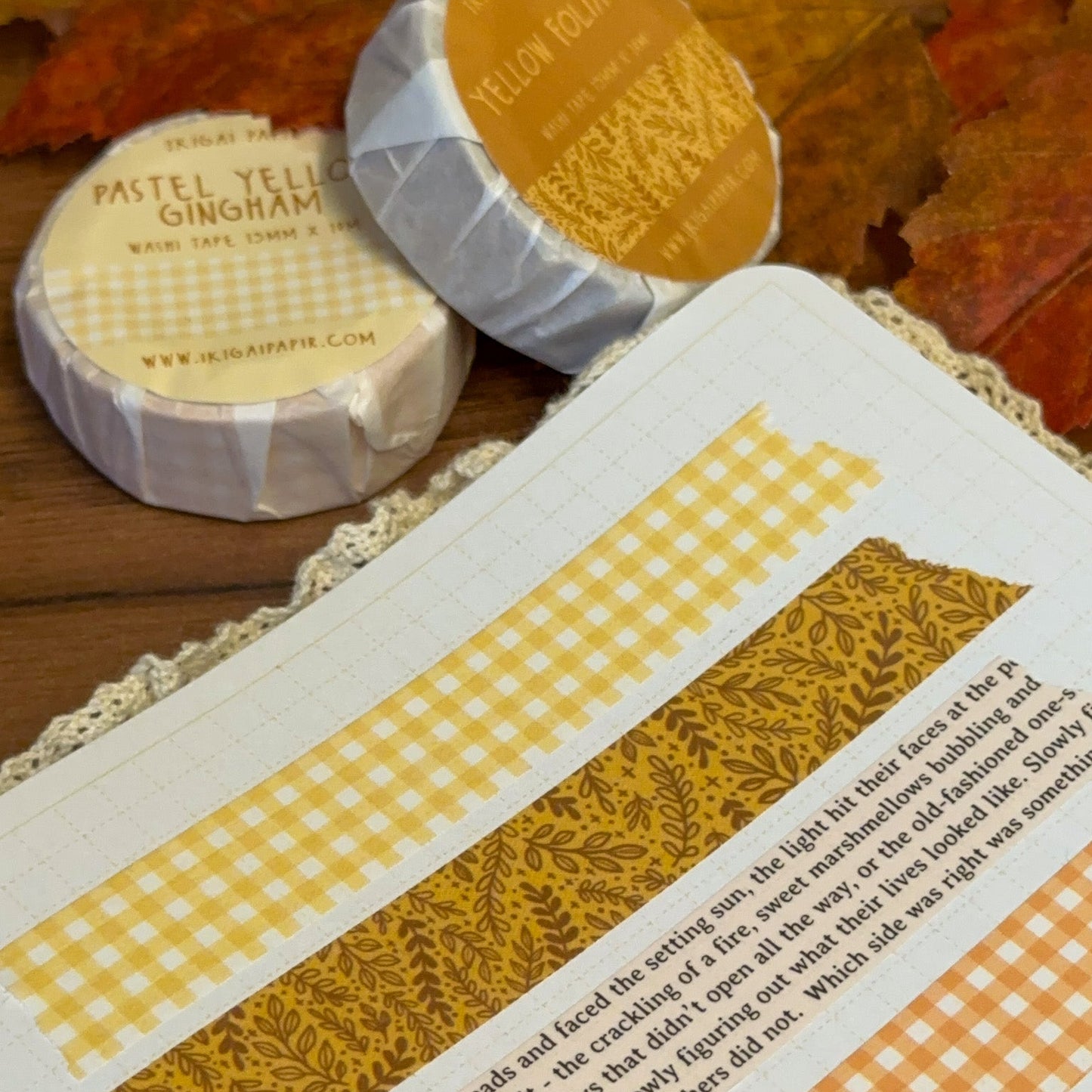 Two rolls of yellow washi tape on a textured surface with autumn leaves.