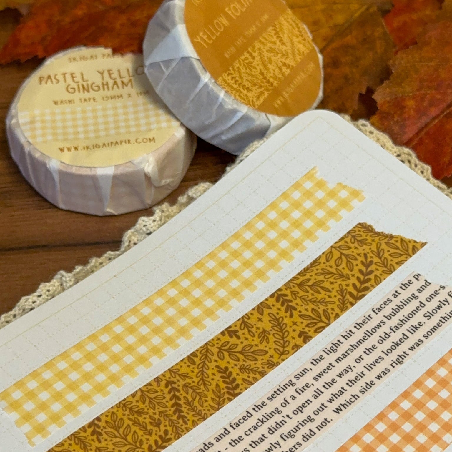 Two rolls of yellow washi tape on a textured surface with autumn leaves.