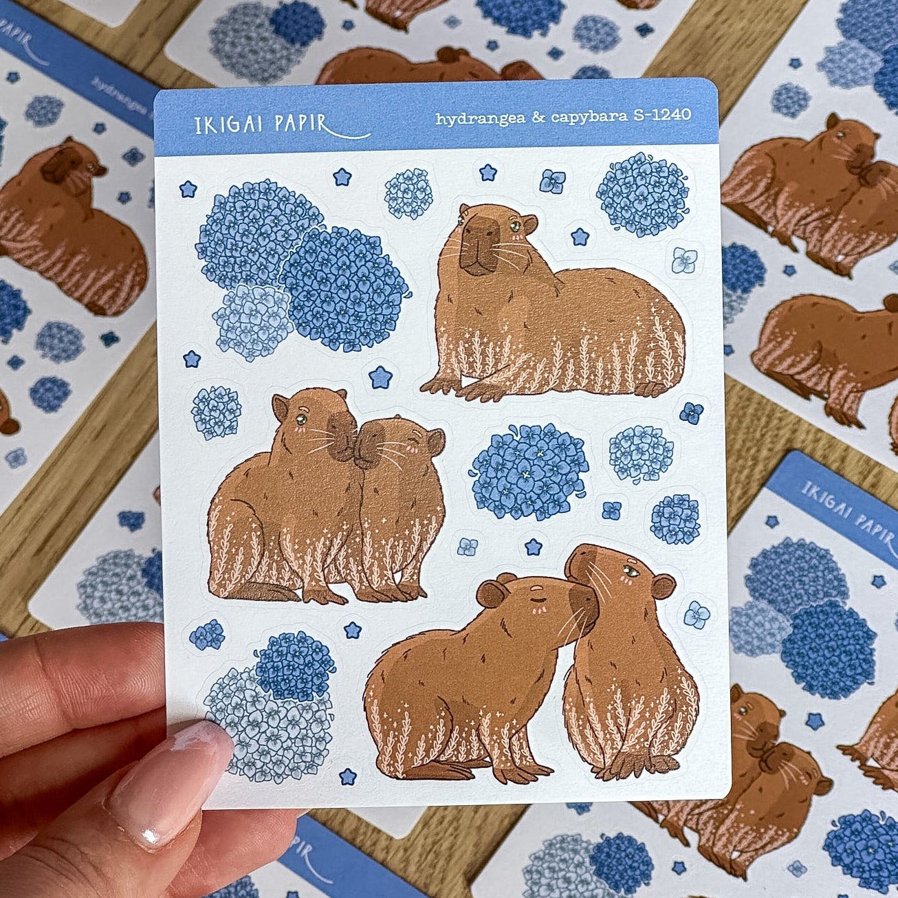 Sheet of capybara stickers held by a hand with more stickers in the background.